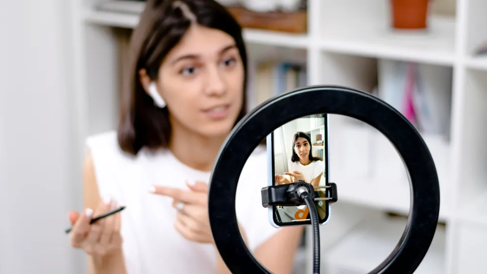 Influencer girl blogger talking smartphone,live recording video blog on social network at home.Social media live streaming concept.Focus on the phone, the girl in the background in a blur.