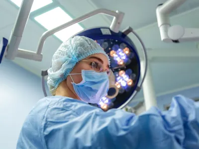 ﻿Female Doctor in Surgery Operating Hospital Room. Surgeon medic in protective work wear gloves, mask and cap.