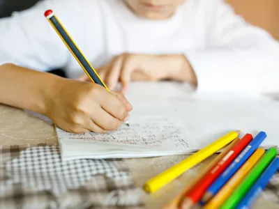 Child doing homework and writing story essay. Elementary or primary school class. Closeup of hands and colorful pencils.