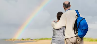 Affectionate aged couple looking at rainbow against grey cloudy sky / Foto: Shironosov
