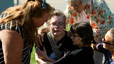 Joanne Green of Fenton, 75, top right, and McKenna Harrington of Davison, 25, second from right, comfort Katelyn Kruse of Fenton, 26, center, after Kruse was present at the scene of a shooting and structure fire at The Church of Jesus Christ of Latter-day Saints on McCandlish Road in Grand Blanc, Mich., Sunday, Sept. 28, 2025. (Katy Kildee/Detroit News via AP)