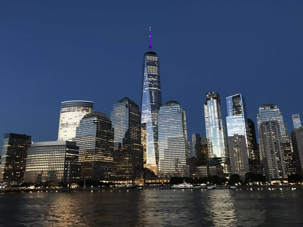 City lights illuminate the cityscape just after sunset in New York City's Financial District. Views from a sunset cruise heading to the Statue of Liberty. Iconic buildings such as One World Trade Center stand tall. / Foto: Katie Desmond