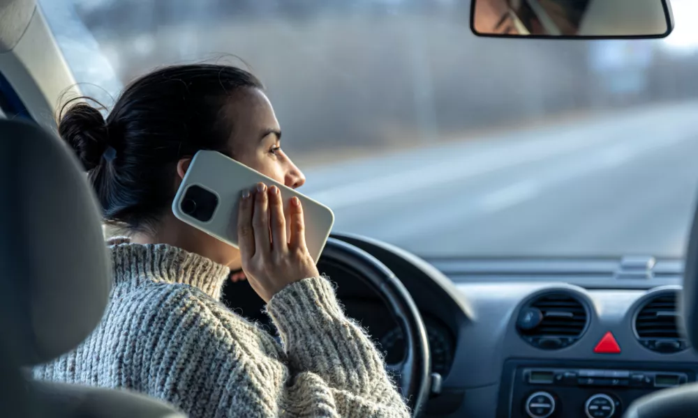 Young woman talking on the phone while driving a car, inside view. / Foto: Puhimec, Getty Images