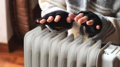 Person heating their hands at home over a domestic portable radiator in winter