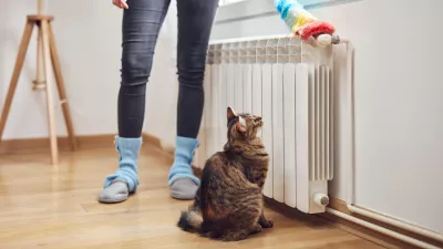 Woman with a dust stick cleaning central heating gas radiator at home. / Foto: M-gucci