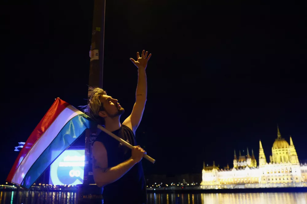 A person holds a flag and gestures as people celebrate following partial results in the Hungarian Parliamentary election in Budapest, Hungary, April 13, 2026. REUTERS/Bernadett Szabo