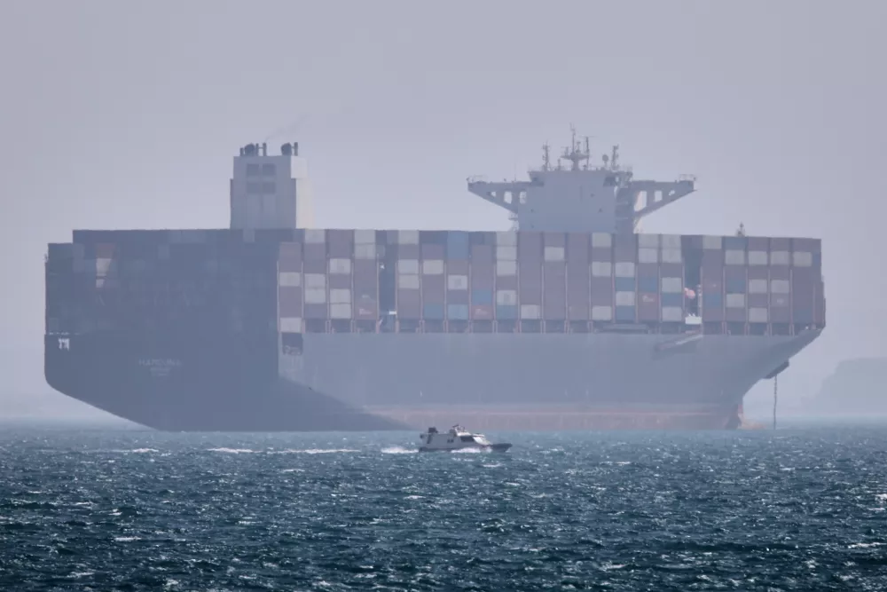A container ship sits at anchor as a small motorboat passes in the foreground in the Strait of Hormuz off Bandar Abbas, Iran, Saturday, May 2, 2026. (Amirhosein Khorgooi/ISNA via AP)