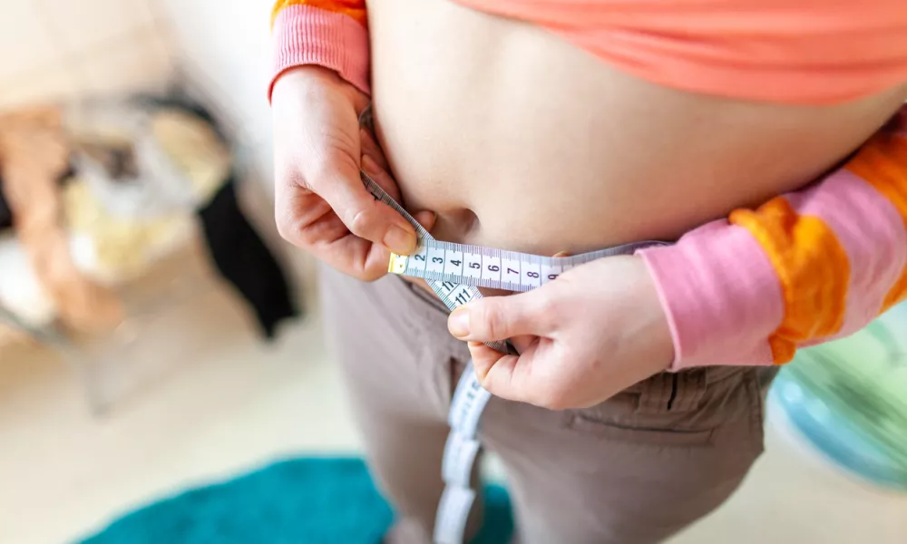 woman measures her abdomen with a measuring tape