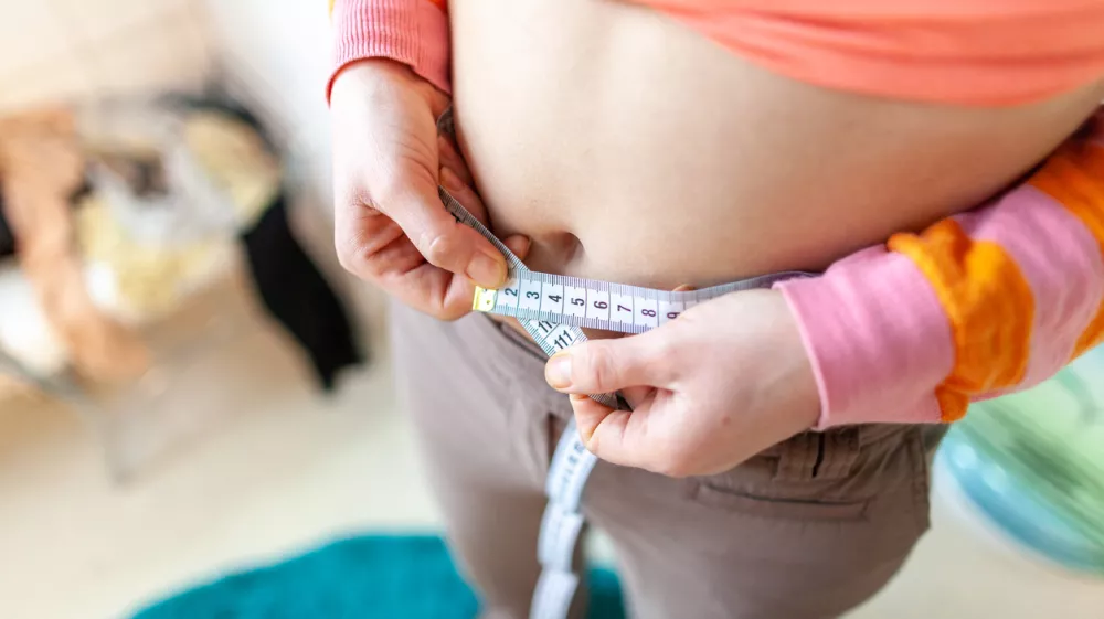 woman measures her abdomen with a measuring tape