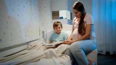 Young pregnant woman in pajamas with her son reading fairytale book at night before going to sleep. Parenting and pregnancy.