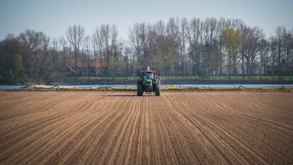 A tractor driving in the middle of arable land against trees and blue sky