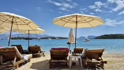 Serene beach scene with wooden loungers and sun umbrellas facing a calm, turquoise sea with boats under a bright blue sky, ideal for summer and vacation themes.