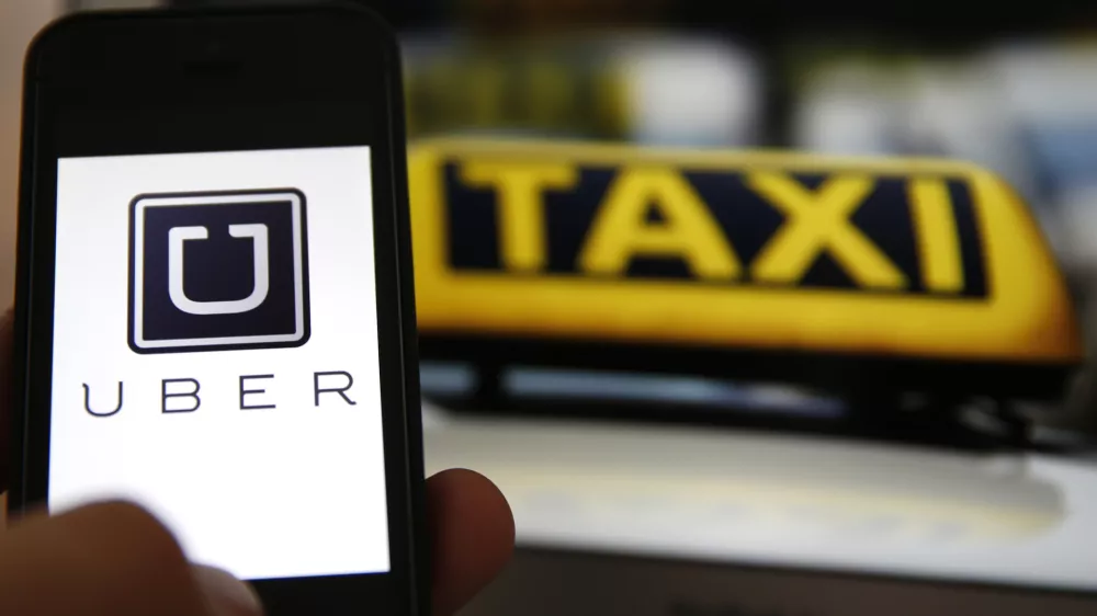 File illustration picture showing the logo of car-sharing service app Uber on a smartphone next to the picture of an official German taxi sign in Frankfurt, September 15, 2014. A Frankfurt court earlier this month instituted a temporary injunction against Uber from offering car-sharing services across Germany. San Francisco-based Uber, which allows users to summon taxi-like services on their smartphones, offers two main services, Uber, its classic low-cost, limousine pick-up service, and Uberpop, a newer ride-sharing service, which connects private drivers to passengers - an established practice in Germany that nonetheless operates in a legal grey area of rules governing commercial transportation.  REUTERS/Kai Pfaffenbach/Files (GERMANY - Tags: BUSINESS EMPLOYMENT CRIME LAW TRANSPORT)