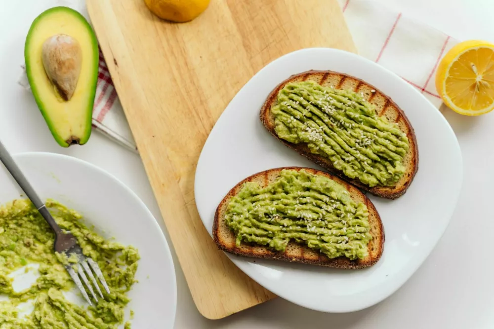 toasted bread with avocado paste. toast with avocado lies on a white plate and wooden cutting board. health food concept, vegan, vegetarian / Foto: Galina Tsyrulnik