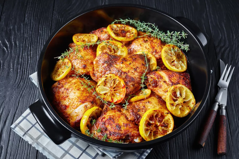 baked Chicken Thighs With Roasted Lemon Slices and thyme in a black ceramic dutch oven on a wooden table, horizontal view from above / Foto: From_my_point_of_view