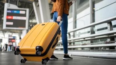 Close up of unrecognized woman tourist walking with her luggage through international airport terminal during holiday trip, female tourist rolling suitcase alone.
