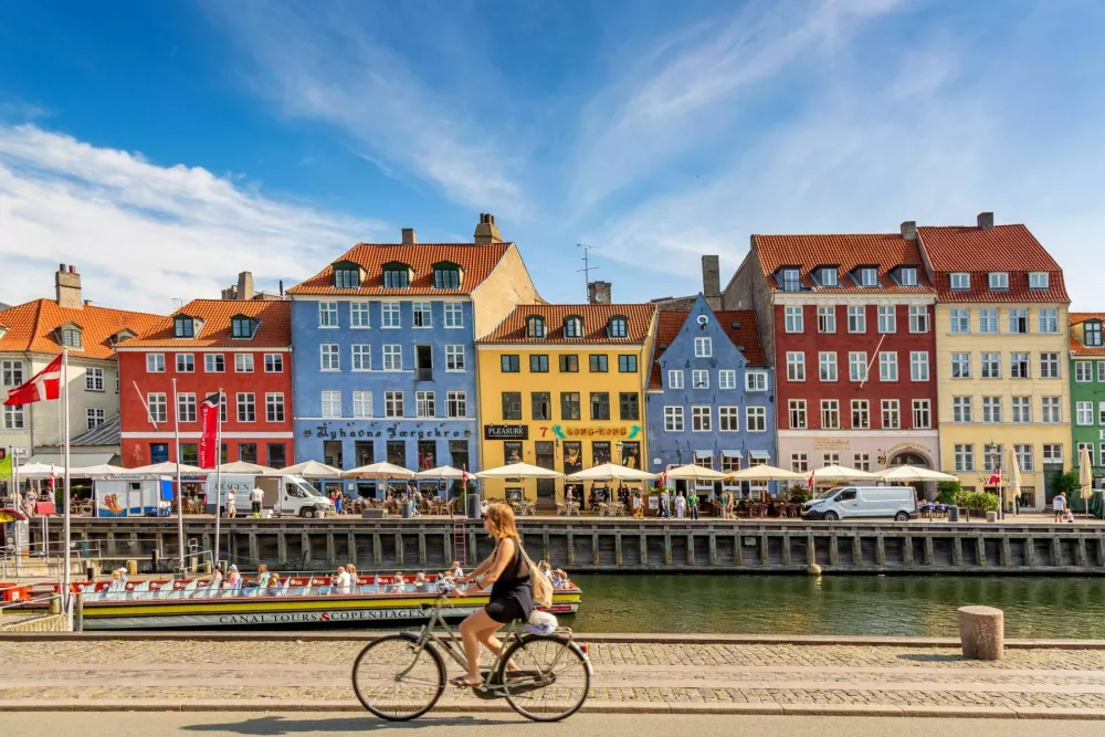 Copenhagen, Denmark - July, 2019: Copenhagen iconic view. Famous old Nyhavn port with colorful medieval houses, tourist ship and woman on a bicycle in the center of Copenhagen. Selective focus. / Foto: Nantonov