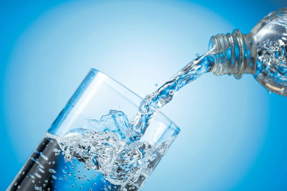 Clear drinking carbonated water pouring into a tall glass from a transparent plastic bottle. Blue backlight, copy space. / Foto: Igorr1