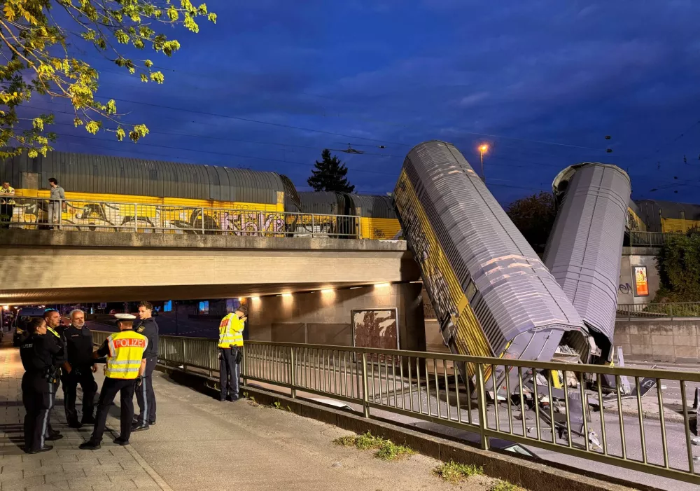 Police talks at the site after two cars of a freight train which derailed following a collision, fell off a bridge and lay on a road in Munich, Germany, June 20, 2026.  REUTERS/Christine Uyanik