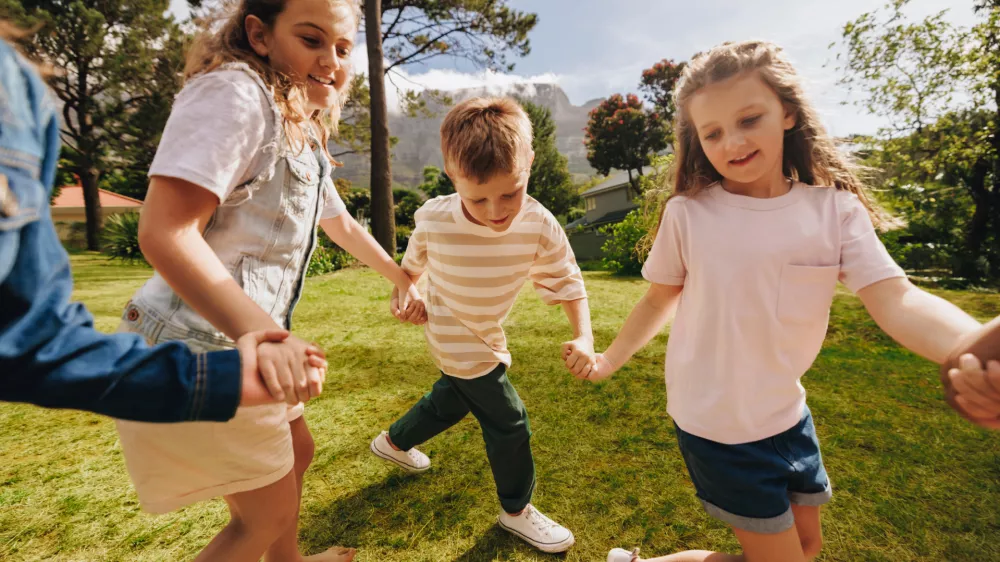 A group of happy children holding hands and playing on a sunny day in a park, enjoying outdoor activities and showcasing friendship, joy, and togetherness in a vibrant and lively environment.
