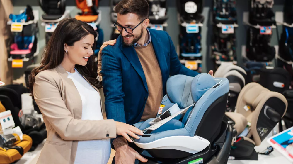 Beautiful couple choosing and buying car safety seat for their baby. Parenthood and child expecting concept.