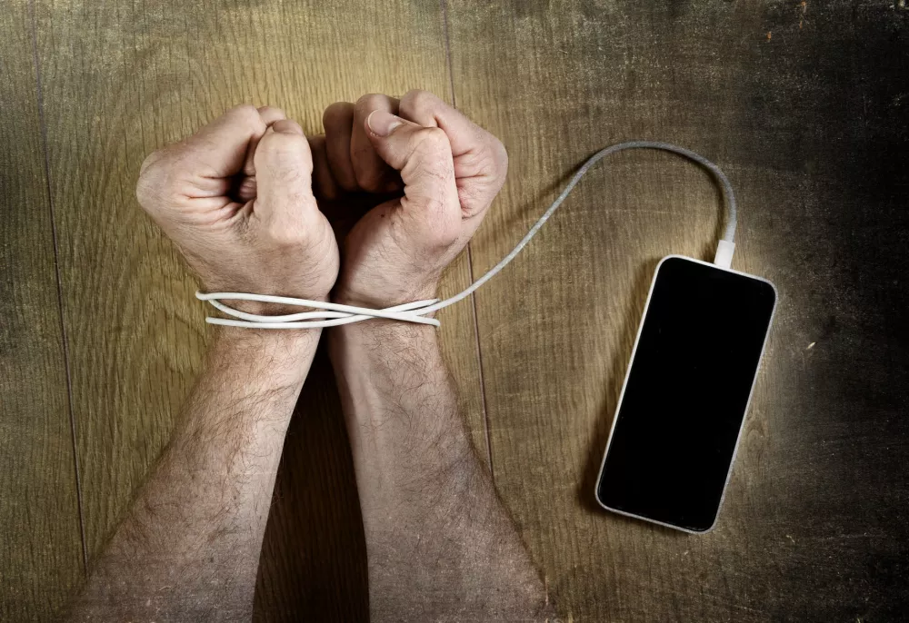 man hands trapped and wrapped on wrists with mobile phone cable as handcuffs in smart phone networking and communication technology addiction concept