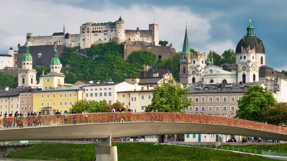 SALZBURG, AUSTRIA - May 4th, 2018: View to Hohensalzburg Fortress and Staatsbruecke bridge across Salzach river on a spring evening with many people walking