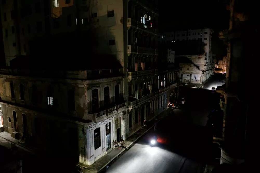 A motorcycle's headlight illuminates a dark street while residents sit outside their apartment buildings as Cuba's national power grid collapsed, marking the third major outage in nine days, in Havana, Cuba, July 14, 2026. REUTERS/Norlys Perez