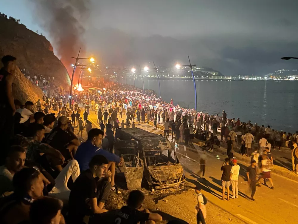 Migrants gather around a torched vehicle while waiting for a chance to cross to the Spanish enclave of Ceuta, on the Moroccan side of the border in Fnideq, Morocco, July 31, 2026. Picture taken with a mobile phone.  REUTERS/Ahmed El Jechtimi