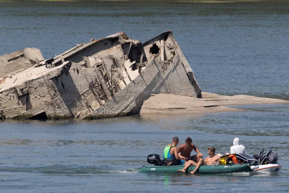 People in a boat pass by a sunken German warship from World War II, exposed due to low Danube River levels caused by drought and extreme heat, in Prahovo, Serbia, July 30, 2026. REUTERS/Djordje Kojadinovic