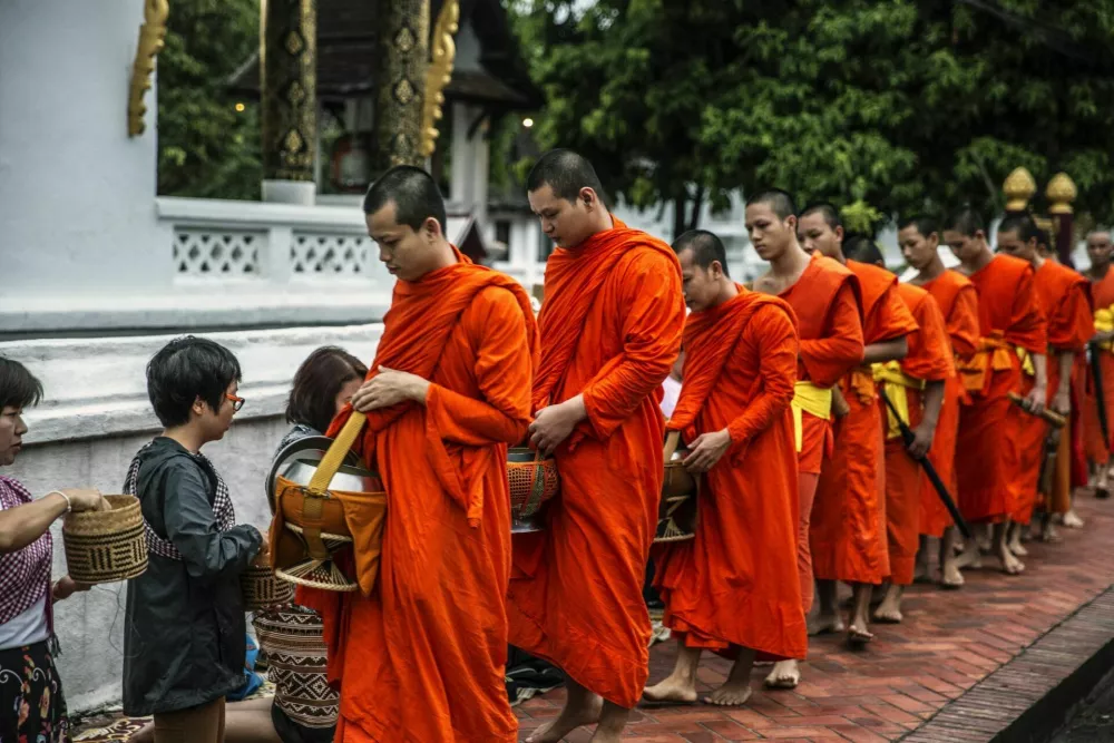Luang Prabang, Laos - July 18, 2015: Luang Prabang, Laos - July 18, 2015: Morning alms in Luang Prabang, known as Tak Bat, is a serene Buddhist ritual. At sunrise, barefoot monks, draped in saffron robes, walk in silence through the streets. This photo encapsulates the moment as visitors graciously offer food and beverages to the monks. / Foto: Wallis Yu