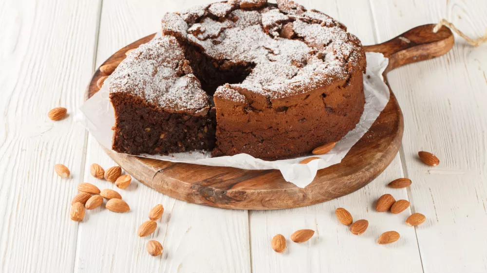 Italian Torta Caprese is a decadent, flourless cake made with dark chocolate and almonds closeup on the wooden board on the table. Horizontal / Foto: Alleko
