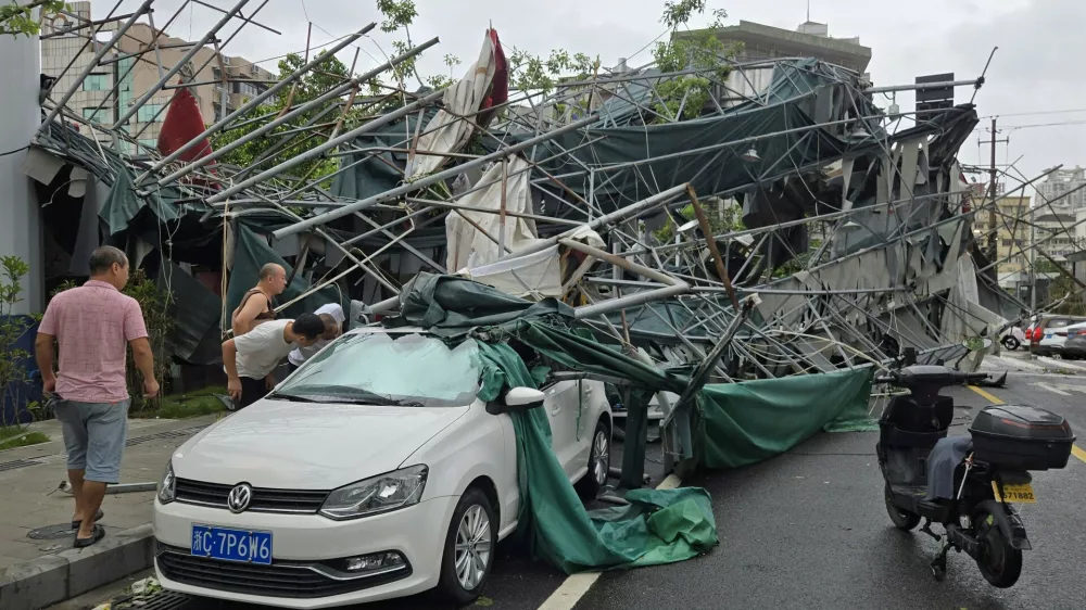 People look inside a car pinned by a fallen scaffolding structure after Typhoon Dolphin affected the area, in Wenzhou in eastern China's Zhejiang province, Monday, Aug. 10, 2026. (Chinatopix Via AP)