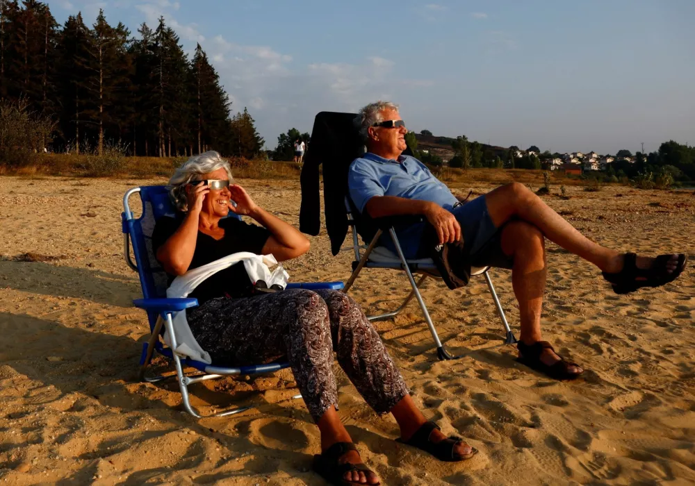 Patricia Molera and Enrique Sotomayor test their eclipse glasses during sunset at Arija beach, Spain, August 11, 2026. REUTERS/Borja Suarez