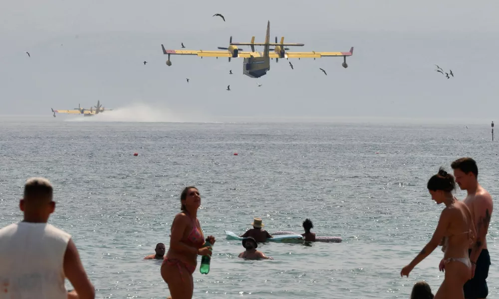 Beachgoers look at the firefighting airplanes scooping water from the Adriatic Sea during a wildfire near Omis, southern Croatia, Friday, Aug. 14, 2026. (AP Photo/Josko Ponos)