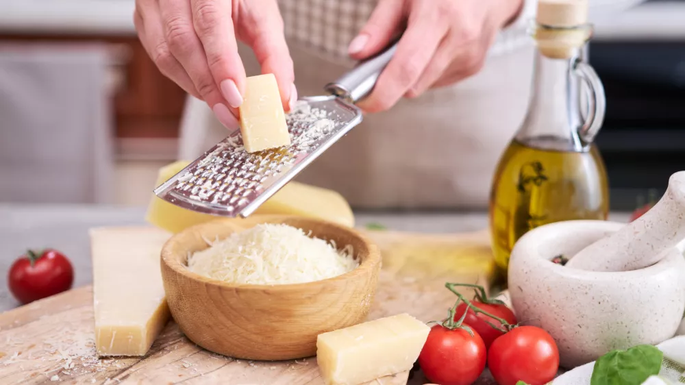 Woman grates Parmesan cheese on a wooden cutting board at domestic kitchen.