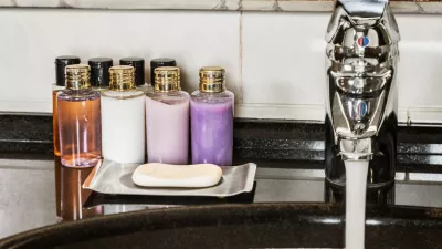 Water flows from the tap in the bathroom. Mini bottles of cosmetics on the table in the hotel room / Foto: Doroo