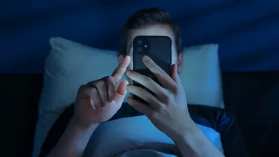 Close up of young man, alone in the dark bedroom, holds his smartphone close to face while scrolling social media or texting late at night. Screen dependence, excessive consumption of content / Foto: Arsenii Palivoda Getty Images