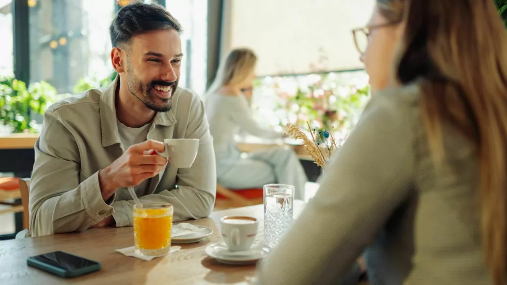 Happy couple sipping coffee and engaging in lively conversation at a cafe, cherishing their time together and enjoying each other's company / Foto: Zamrznutitonovi