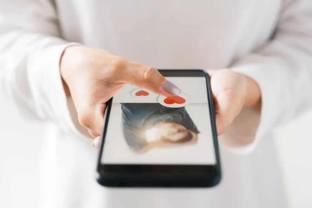 Valentine's day and love day concept, woman finger touching heart icon on screen in smartphone application, happy woman posting love heart emoji icon button, search app Online couple. / Foto: Thapana Onphalai Getty Images/istockphoto