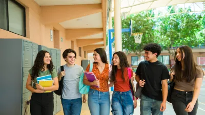 Group of cheerful latin teenage students walking together in school hallway and carrying backpacks and notebooks