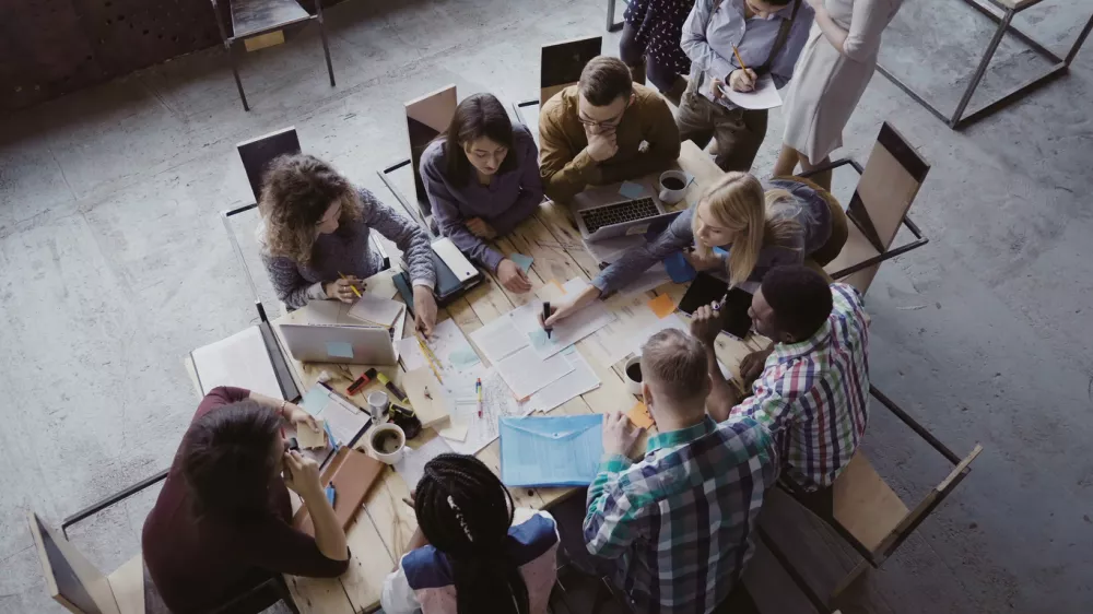 Top view of creative business team sitting at the table at loft office and working. Woman manager brings the document to mixed race group of people. Colleagues discussing the project.