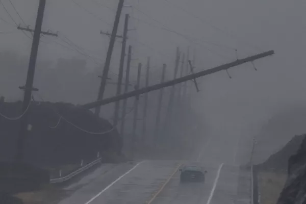 A vehicle drives near a downed utility pole dangling above Mamalahoa Highway during Hurricane Lala near Ocean View, Hawaii, Saturday, Aug. 15, 2026. (Stephen Lam/San Francisco Chronicle via AP)