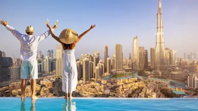 A happy tourist couple on vacation time stands by the pool edge and enjoys the panoramic sunset view of the Dubai city skyline, UAE