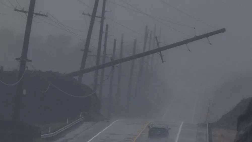 A vehicle drives near a downed utility pole dangling above Mamalahoa Highway during Hurricane Lala near Ocean View, Hawaii, Saturday, Aug. 15, 2026. (Stephen Lam/San Francisco Chronicle via AP)