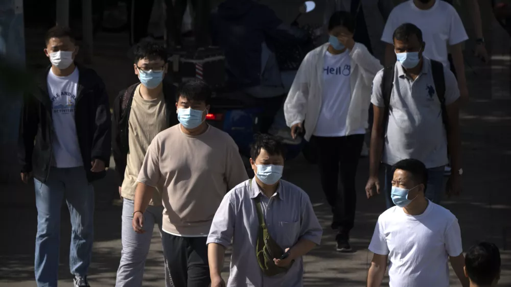 Commuters wearing face masks walk along a street during the morning rush hour in Beijing, Tuesday, May 23, 2023. (AP Photo/Mark Schiefelbein)
