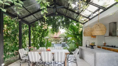 Open kitchen with empty dining room table and chairs outside, against green fresh plants on background