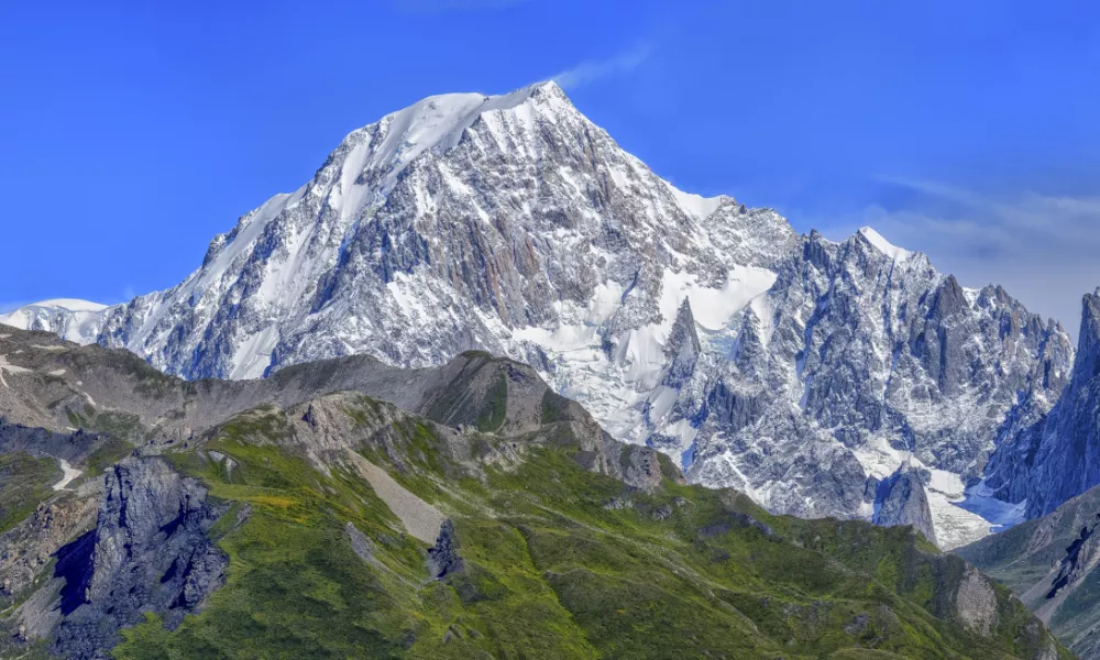 Panoramic view of snow-capped mountains and green valleys under a clear blue sky