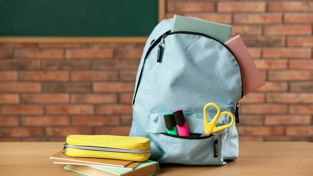 Light blue backpack with different stationery, pencil case and book on desk in classroom / Foto: Olga Yastremska