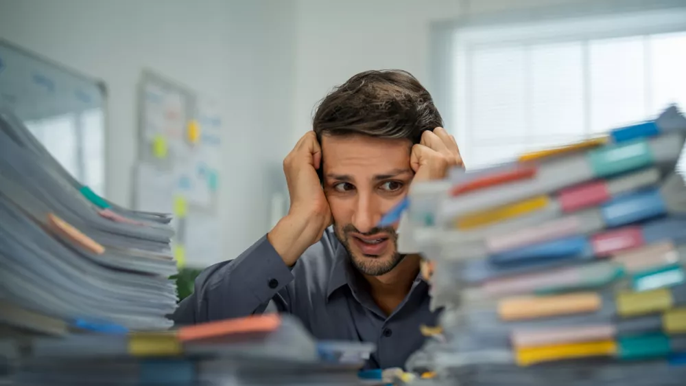 Tired Hispanic employee dealing with overwhelming workloads indoors, experiencing anxiety and pain from work-related challenges and deadlines.